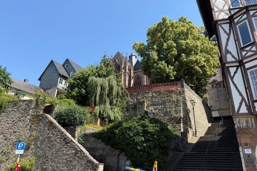 A historic stone wall with a staircase, a tree, and traditional half-timbered buildings. 2