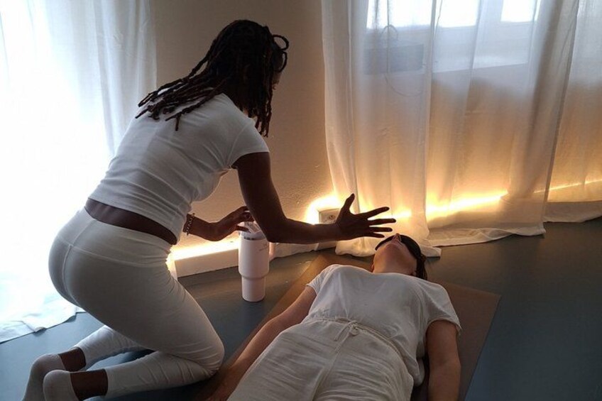 A person performing a massage on another individual in a room with a yoga mat, a water bottle, and sheer curtains. 4