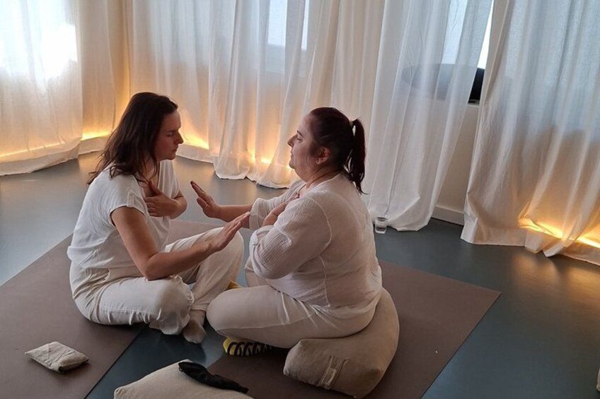 Two people sitting on yoga mats in a room with white curtains. 5