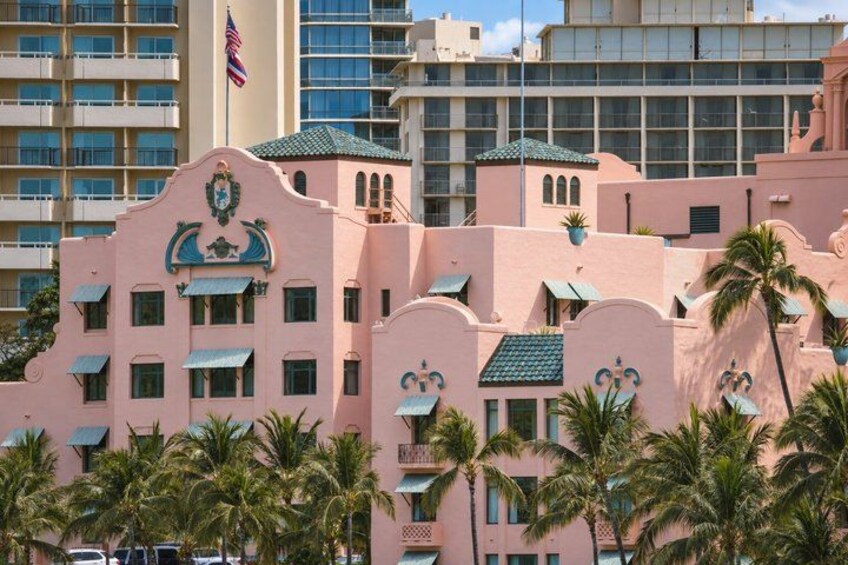 A pink building with a green roof, palm trees, and a flag. 5
