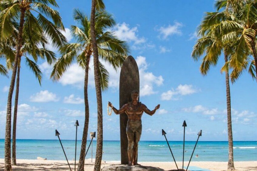 A statue of a person with a surfboard, surrounded by palm trees and the ocean. 2