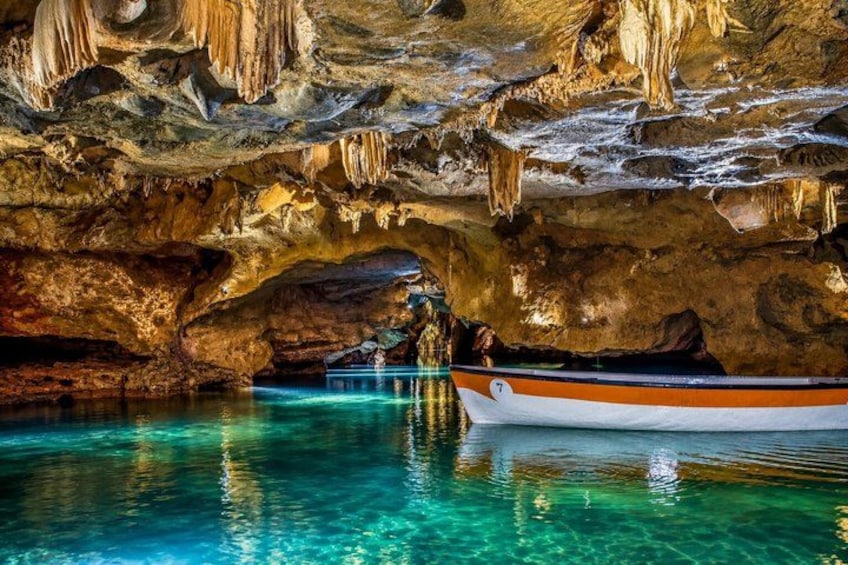 A boat on a clear blue water body under a cave with stalactites. 1
