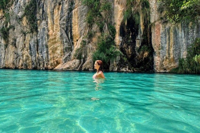 A person swimming in clear turquoise water with rocky cliffs in the background. 2