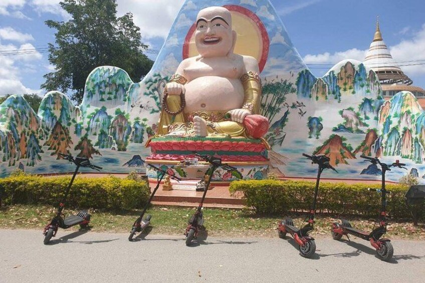 A large Buddha statue with a mural backdrop, surrounded by electric scooters. 4