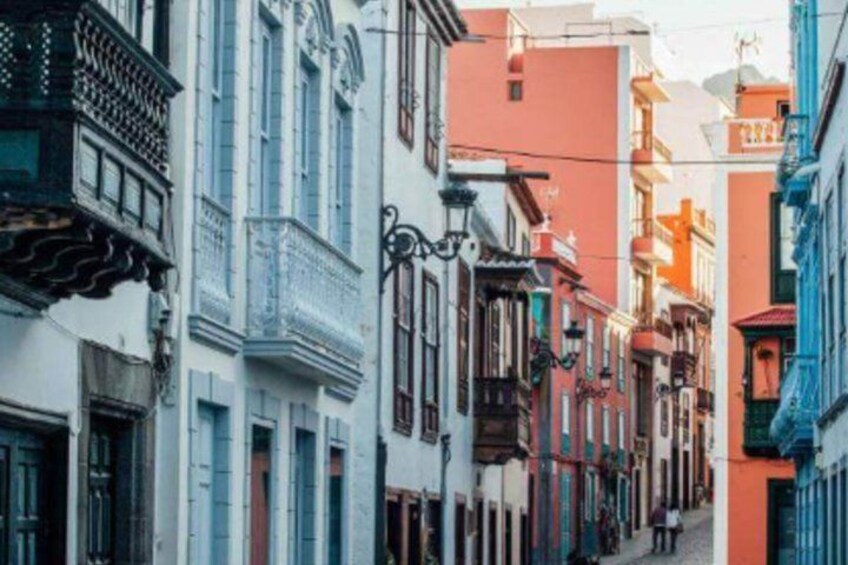 A narrow street lined with colorful buildings, some with balconies and decorative railings. 2