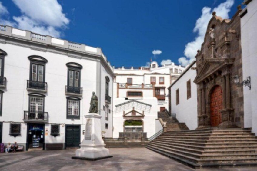 A plaza with a statue, white buildings, and a church with a red door. 4