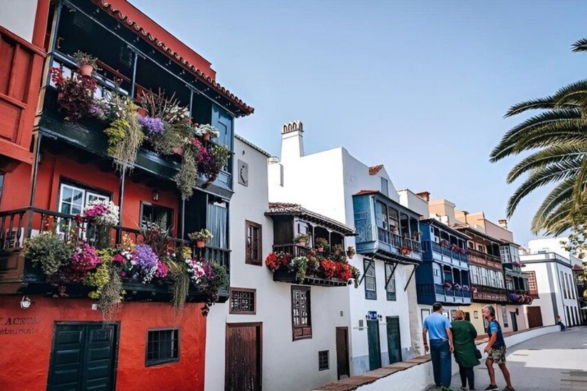 Colorful buildings with balconies adorned with flowers, a clear sky, and a palm tree. 1