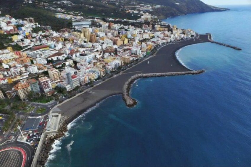 A coastal city with a curved road leading to the sea, a rocky breakwater, and dense urban buildings. 3