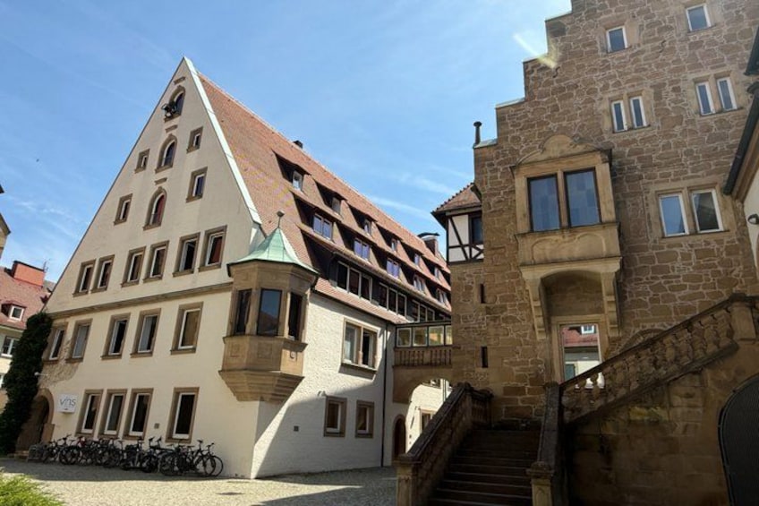A historic building with a steeply pitched roof, a tower, and a staircase leading to an upper level. 4