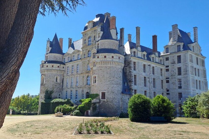 A large stone castle with multiple towers and turrets, surrounded by well-maintained gardens and a clear blue sky. 1