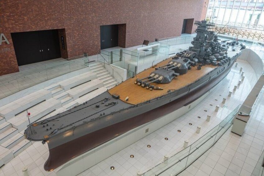 A large naval ship on display in a museum with a tiled floor and glass railings. 1