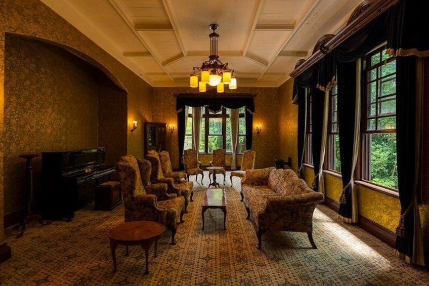 A room with a large chandelier, a fireplace, and a view of trees through the windows. 3