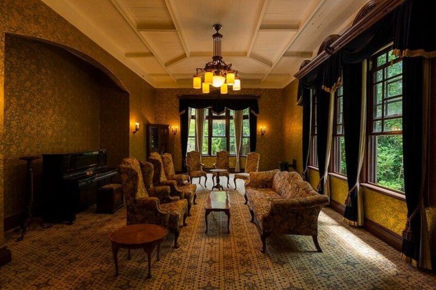 A room with a large chandelier, a fireplace, and a view of trees through the windows. 2