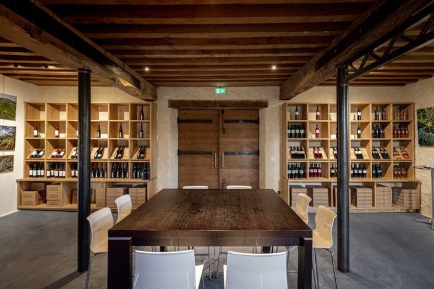 A wooden table with chairs, surrounded by shelves of wine bottles. 2