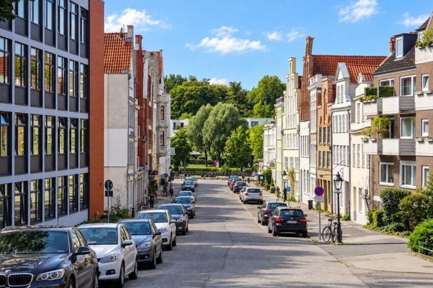 A street lined with parked cars and buildings, a bicycle, and a clear blue sky. 5
