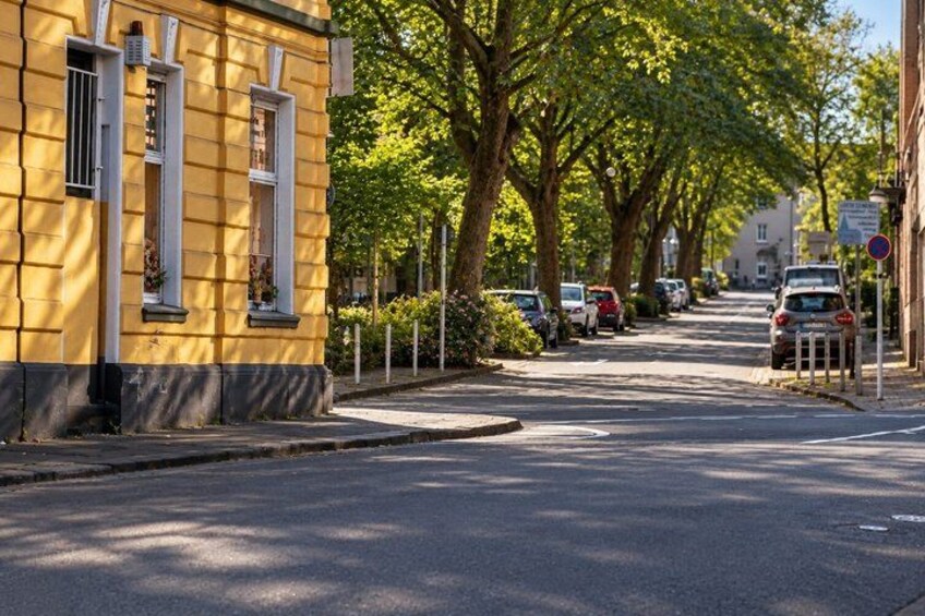 A yellow building with white shutters, parked cars, and trees lining a street. 4