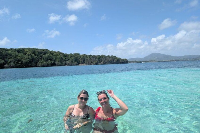 Two people in clear turquoise water with a forested island in the background. 5