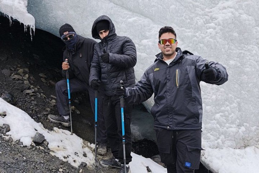 Two people in winter gear standing near a glacier with ice formations. 1