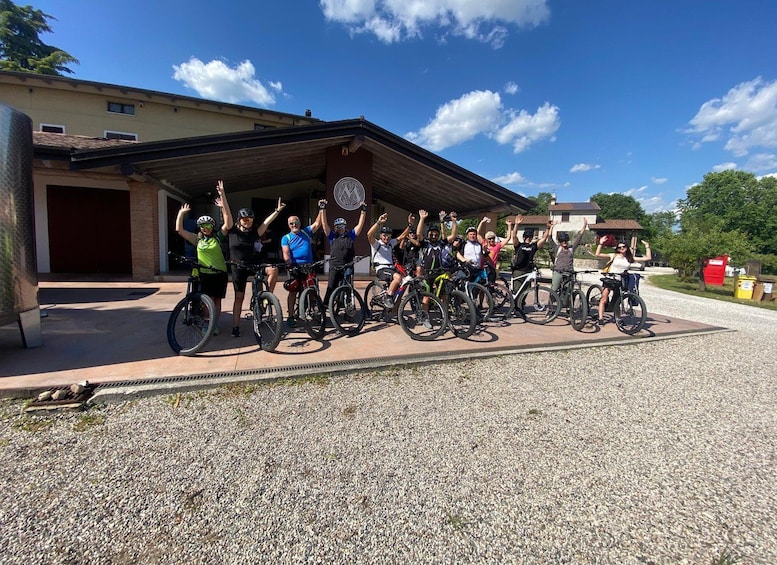 En gruppe cyklister poserer foran en bygning med grusvej. 3