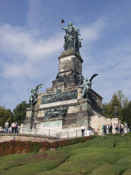 A large bronze statue with multiple figures, surrounded by a landscaped area with trees and a fence. 3