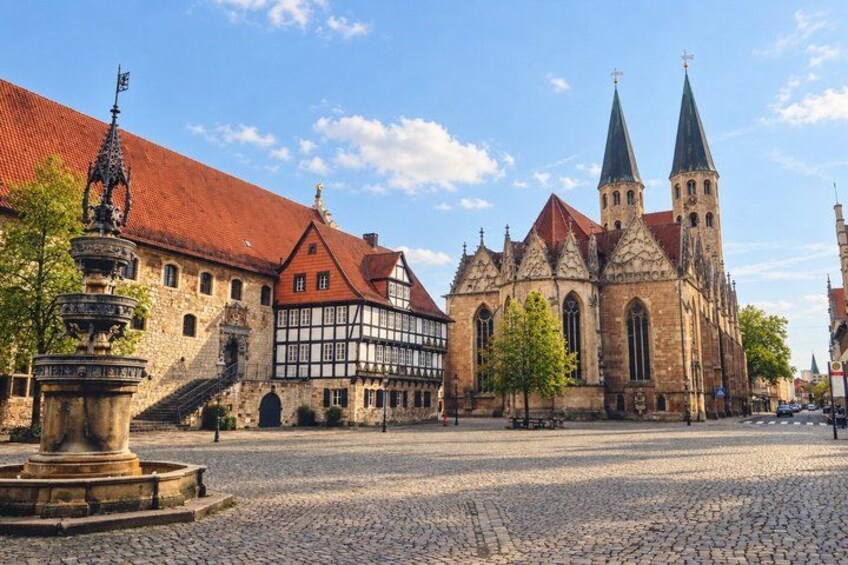 A cobblestone square with historic buildings, including a church with two spires and a half-timbered house. 3
