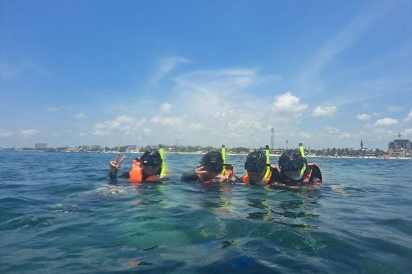 Three people snorkeling in clear blue water with a city skyline in the background. 5