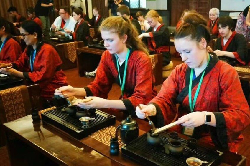 People in red robes preparing tea at tables with teapots and cups. 1