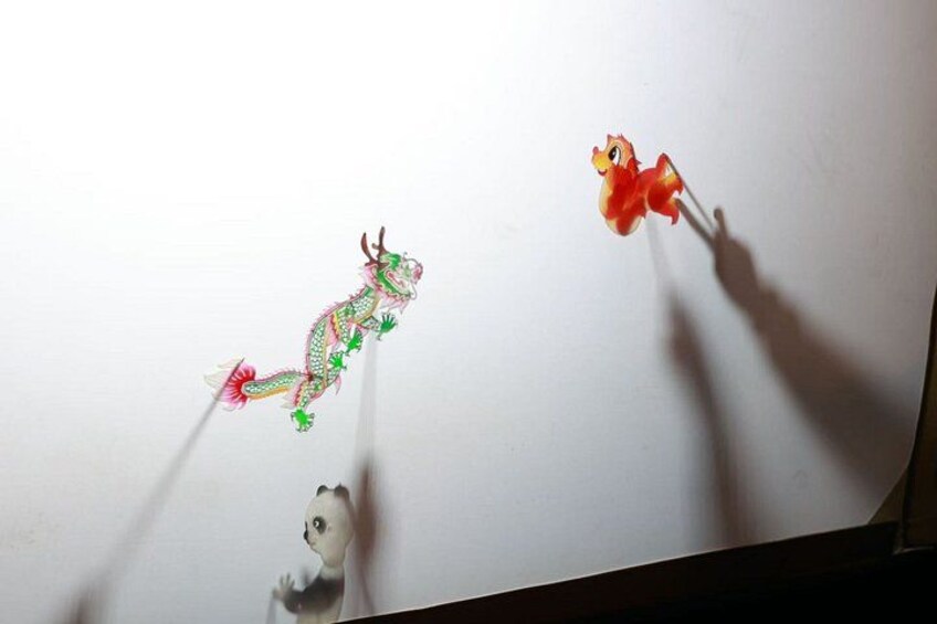 A dragon puppet, a small red figure, and a panda figure on a white surface. 2