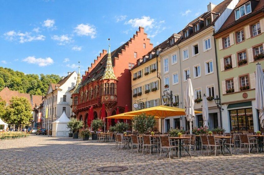 A cobblestone square with historic buildings, outdoor seating, and a church with a spire. 5
