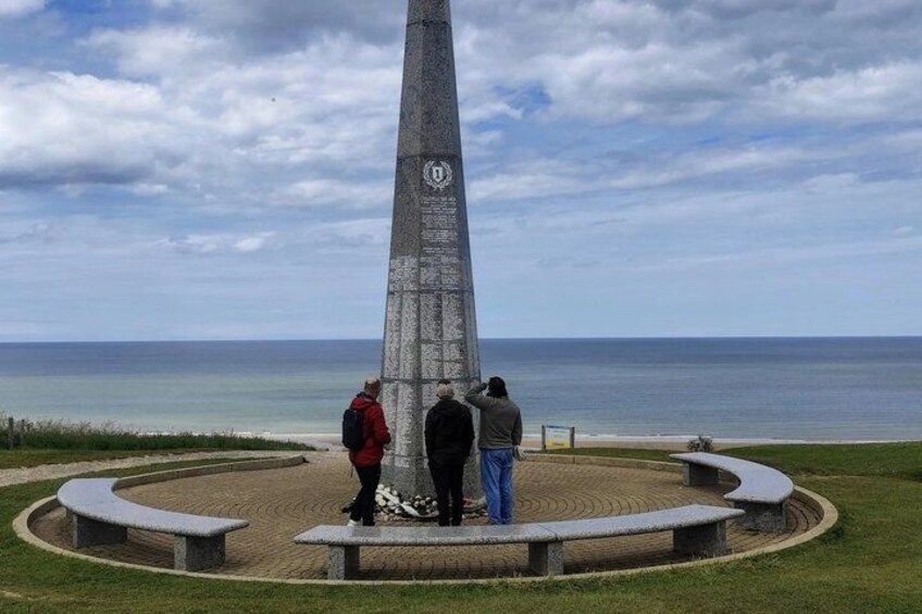 A tall monument with inscriptions, surrounded by a circular stone bench area, overlooking a body of water. 5