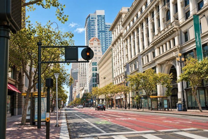 A city street with tram tracks, buildings, and trees. 2