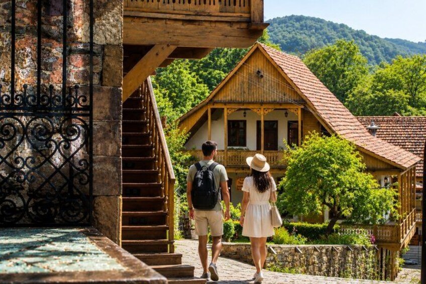 A wooden staircase leading to a traditional house with a red roof, surrounded by greenery and hills. 3