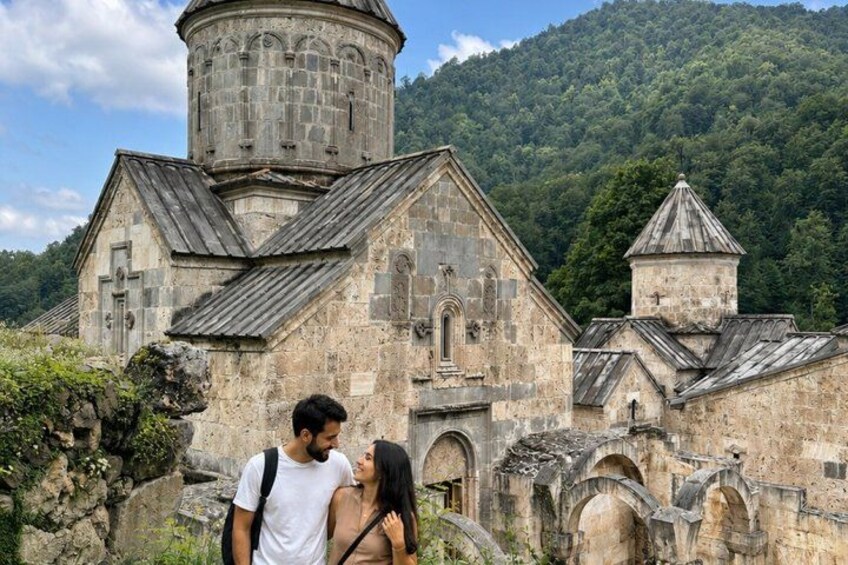 An ancient stone church with a bell tower, surrounded by lush greenery and hills. 1