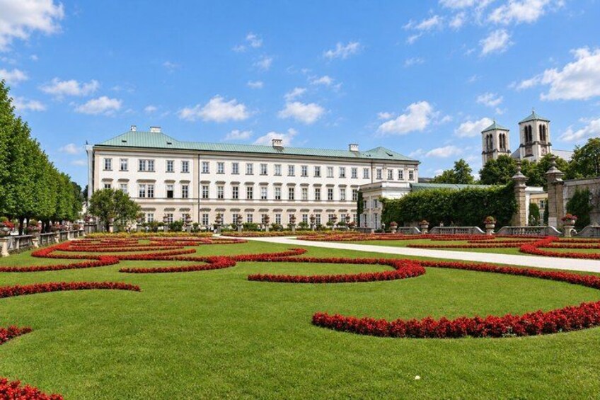 A large building with a green roof, surrounded by a well-manicured garden with red flowers and a clear blue sky. 4