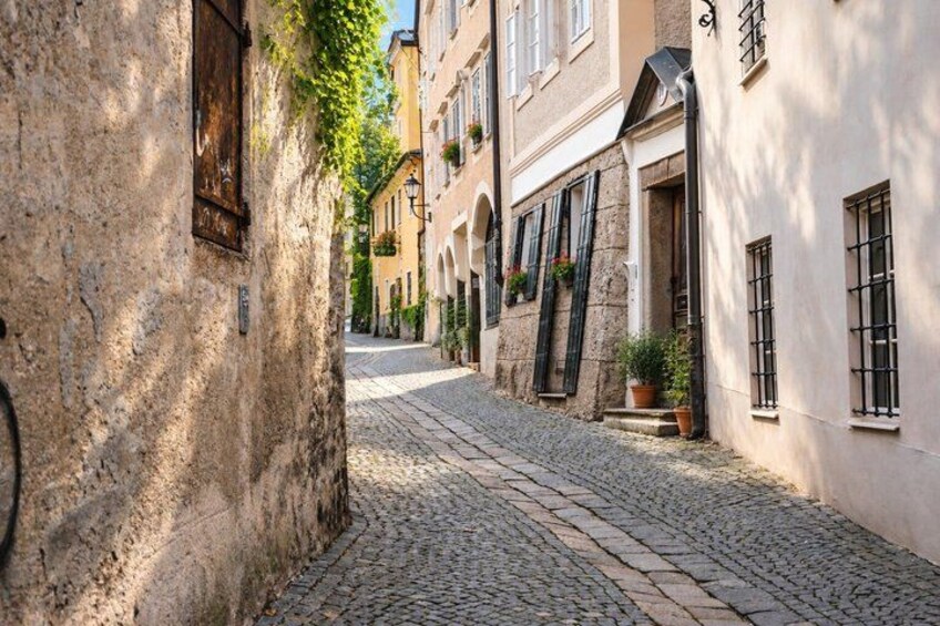 A cobblestone street lined with historic buildings, some with shutters and potted plants. 2