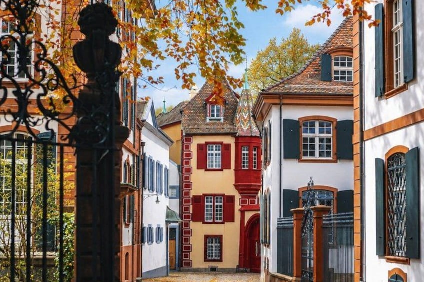 A narrow street with colorful buildings, a wrought iron gate, and autumn leaves. 4