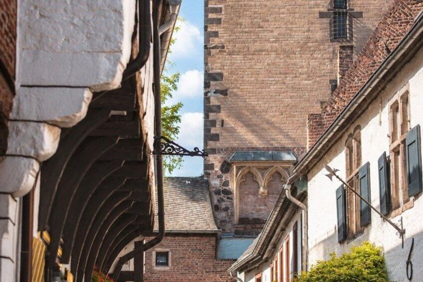 A narrow street with a brick building, a white building with a curved roof, and a large tower in the background. 5