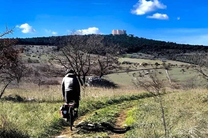A hiker on a trail with a mountainous landscape and a distant building. 1