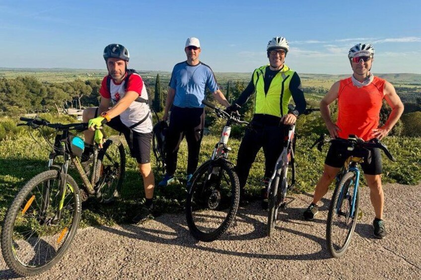 Four cyclists on a gravel path with bicycles, surrounded by greenery and a clear sky. 3