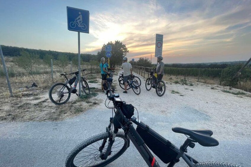 A gravel path with bicycles, a blue bicycle sign, and a sunset in the background. 4