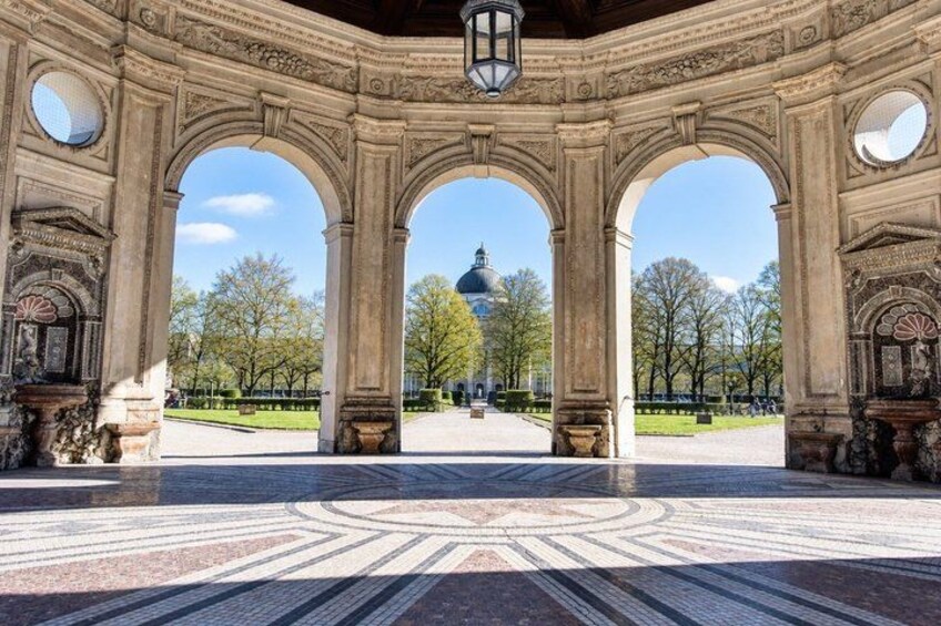 An ornate pavilion with three arches, a patterned floor, and a distant dome structure. 3