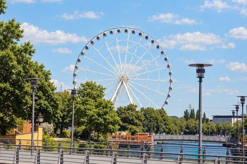 A large Ferris wheel, a body of water, and a bridge in a park. 2