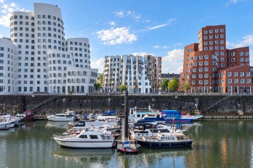 A marina with boats docked, a waterfront promenade, and modern buildings in the background. 2
