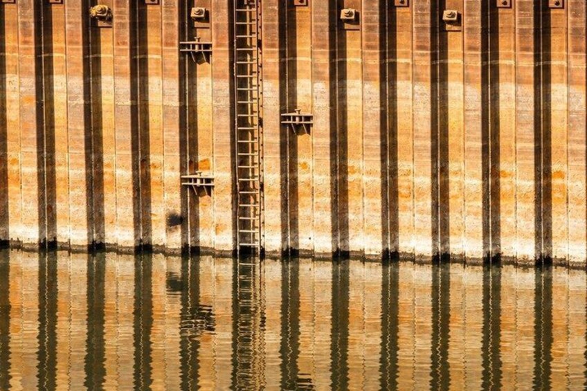 A water body reflecting a brick wall with vertical lines and a ladder. 5