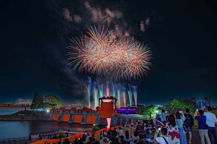A fireworks display over a body of water with a crowd watching. 4
