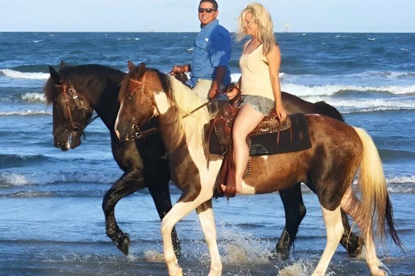 Two horses with riders walking along a beach with ocean waves in the background. 4