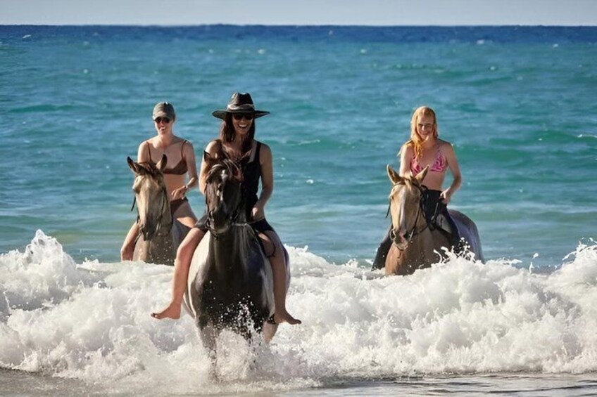 People riding horses on a beach with waves crashing onto the shore. 5