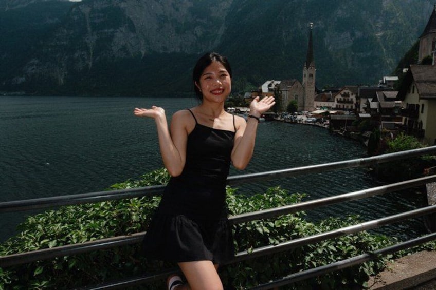 A person in a black dress standing by a railing with a lake and buildings in the background. 2