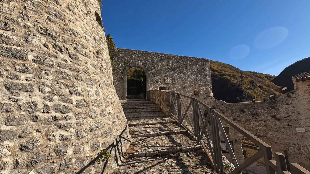 A stone pathway leading through an arched doorway, flanked by stone walls and a wooden railing. 5