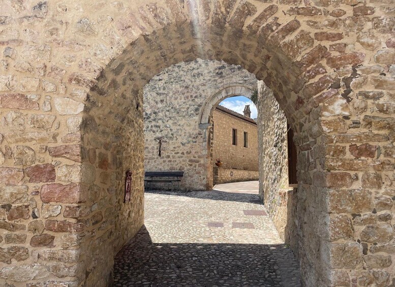 An arched stone passageway with a cobblestone path leading to a building with a tiled roof. 1